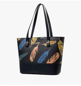 Detail view of black tote bag featuring colorful feather print and golden hardware