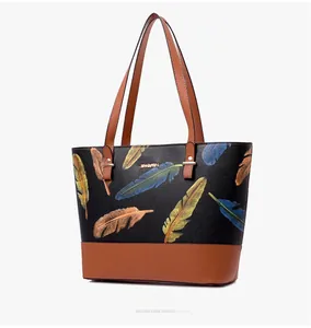 Detail of black pebbled leather tote bag featuring vibrant feather print and metal logo
