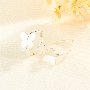 Pair of silver butterfly hoop earrings with polished finish on a soft fabric backdrop