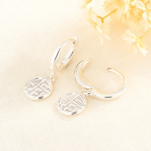 Silver Chinese Fu character earrings with circular pendants on a warm textured background