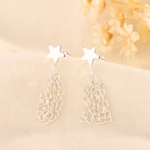 Gros plan de boucles d'oreilles étoiles avec pompons à chaînes sur tissu doux