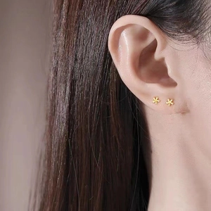 Minimalist golden flower stud earrings for women shown worn on ear in a close-up shot