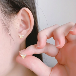 Close-up of golden dragonfly earrings with white marquise-cut stones on a model's ear