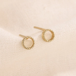 Vue macro de boucles d'oreilles minimalistes en or avec perlage sur fond en tissu doux