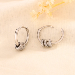 Close-up of silver hoop earrings with zircon beads on a minimalist fabric background