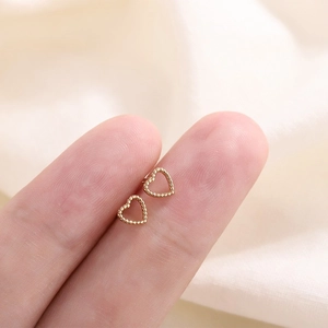 Gros plan de mini boucles d'oreilles cœurs dorés avec texture perlée sur le bout des doigts