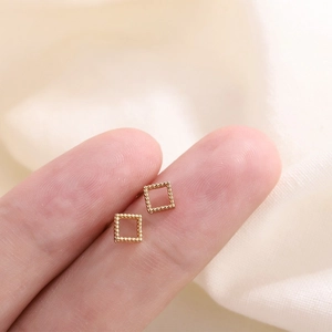 Gros plan de boucles d'oreilles carrées dorées avec texture perlée sur le doigt