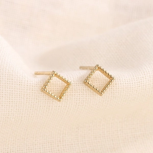 Gros plan de boucles d'oreilles carrées dorées avec bord perlé sur tissu texturé