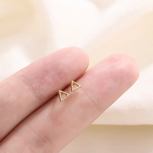Vue macro de petites boucles d'oreilles triangles évidés dorés entre les doigts