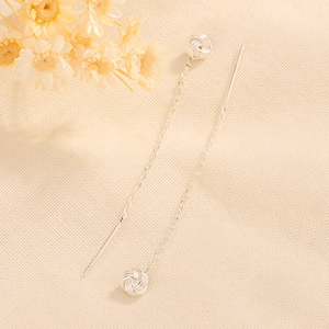 Detail of silver knot tassel earrings with long chain on textured fabric background