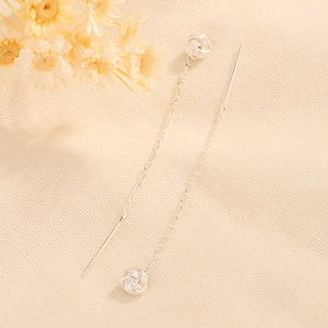 Elegant silver tassel threader earrings with knot charm on a textured fabric background