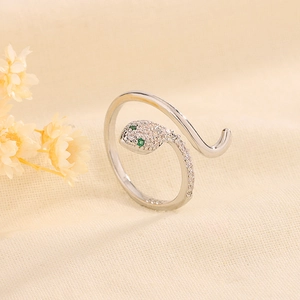 Détail macro d'une bague serpent argentée avec des yeux en zircon vert sur du lin