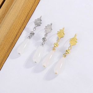 Detail of white drop pearls with gold and silver shell-shaped metal earring pendants