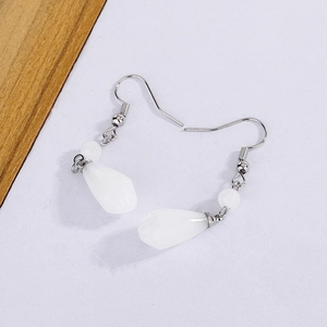 Detail of white teardrop tassel earrings with silver hooks on a wooden and white background