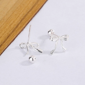 Détail de boucles d'oreilles nœud en argent avec fermoirs à vis sur bloc de bois