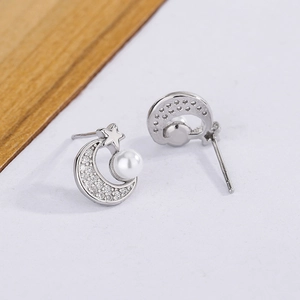 Close-up of star and moon pearl earrings with sparkling cubic zirconia on white surface