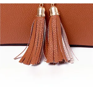 Close-up of brown pebbled leather texture featuring decorative double tassels with gold hardware