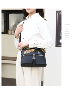 Close-up of black leather tote bag with vibrant feather prints and tassel charm on strap