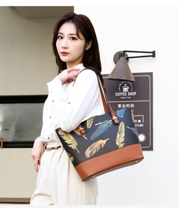 Detailed view of women's tote bag with feather print and brown leather handles on shoulder