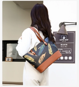 Detailed view of black leather tote bag with colorful feather print on a female model