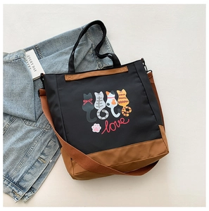 Detail of cartoon cat printed tote bag with brown straps and blue denim jacket background