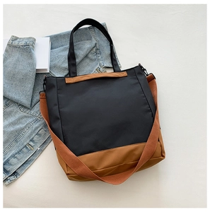 Detail of a color-block tote bag featuring black and brown panels with a wide shoulder strap