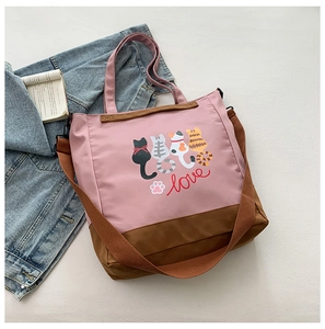Detail of pink canvas tote with cartoon cats and adjustable shoulder strap on gray background