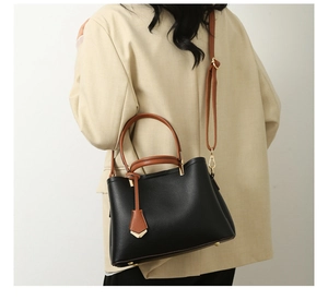 Detail of black tote bag with litchi texture and brown straps on a blazer model