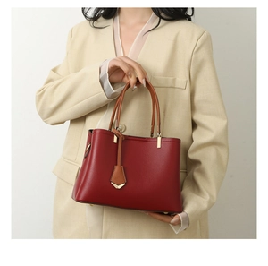 Detail of red pebble leather handbag with brown handles and gold hardware held by model