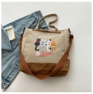 Top view of a beige canvas tote bag with cartoon cat prints and adjustable shoulder strap