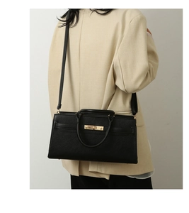 Detail of black pebbled leather handbag with gold twist lock and adjustable shoulder strap
