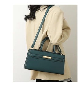Detail of dark teal tote bag with lychee texture and gold metal clasp on a beige blazer