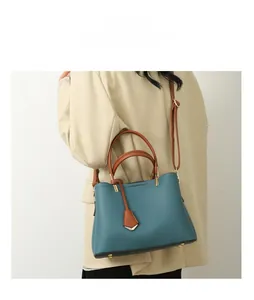 Blue lychee leather handbag with brown handles and gold studs worn by a model in a suit