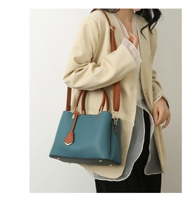 Detail view of teal pebbled leather tote with brown straps and golden protective studs