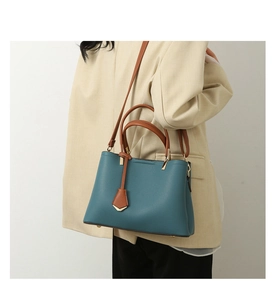 Close-up of blue pebbled leather tote bag worn by model in beige suit jacket