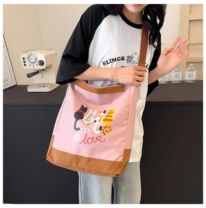 Detail of pink canvas crossbody bag featuring cute cartoon cat prints and brown strap