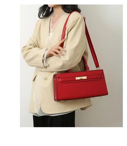 Detailed view of red textured leather tote bag with gold twist lock on a white blazer model
