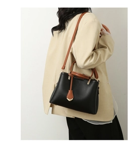 Side view of a black pebbled leather handbag with brown straps worn by a model