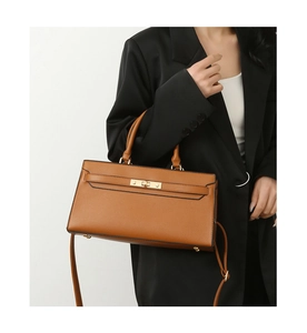 Brown lychee leather handbag with golden twist lock and adjustable shoulder strap worn by model