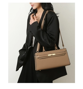 Detailed close-up of brown pebbled leather handbag with gold twist lock on black suit blazer