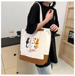Detail shot of a canvas tote bag with cartoon cat illustrations and faux leather straps