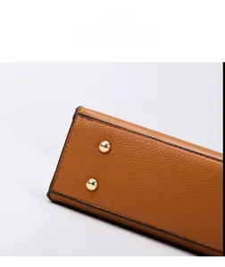 Macro view of brown lychee grain leather tote bag with golden metal bottom studs