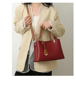 Burgundy grainy leather tote bag with round brown handles held by a model in a beige suit