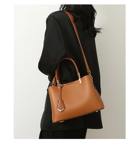 Close-up of brown pebbled leather tote bag with gold hardware worn by model in a black blazer