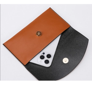 Detail of a brown and black faux leather envelope bag with a round gold magnetic clasp