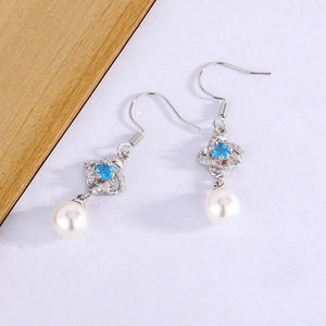 Macro view of silver four-leaf clover earrings with blue gemstone and white pearl drop