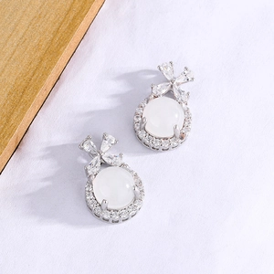 Close-up of silver bow earrings with white chalcedony stone and zircon inlay