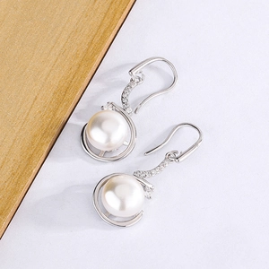 Vue macro de boucles d'oreilles perles blanches avec accents en zircon sur crochets argent