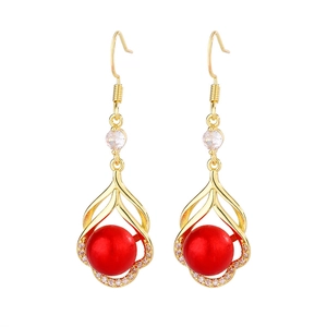 Détail de boucles d'oreilles gouttes dorées avec perles rouges et zircons blancs