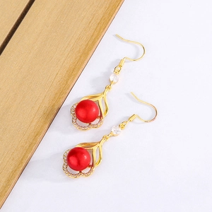 Boucles d'oreilles fleuries dorées avec perles rouges et zircon sur fond bois et blanc